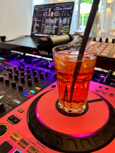 Ein Glas mit Aperol Spritz steht auf einem DJ-Pult mit Lichtern.