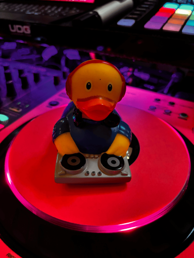 Ein gelber Gummiente als DJ an einem Plattenteller mit bunten Lichtern im Hintergrund.