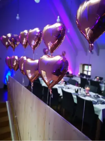Roségoldene Herzballons hängen über einem festlich gedeckten Tisch.
