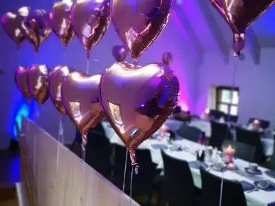 Rosa Herzluftballons hängen über einem festlich gedeckten Tisch.