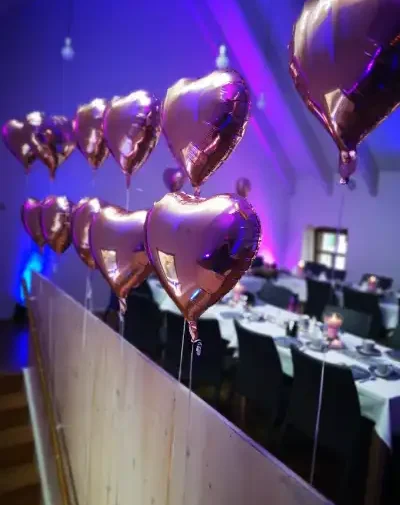 Roségoldene Herzballons hängen über einem festlich gedeckten Tisch.
