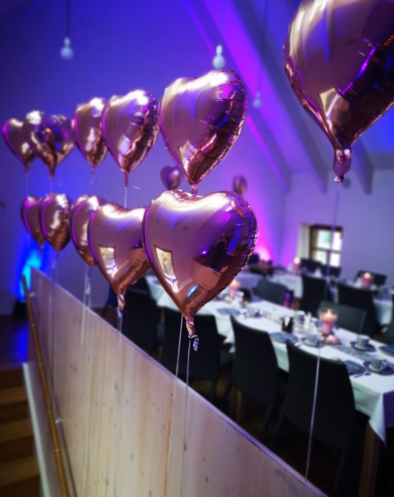 Roségoldene Herzballons hängen über einem festlich gedeckten Tisch.