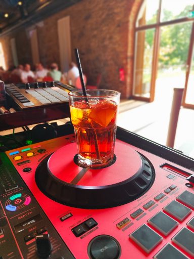 Ein Getränk in einem Glas auf einem DJ-Pult, im Hintergrund eine helle, einladende Umgebung. Photo by DJ Mirko Anders