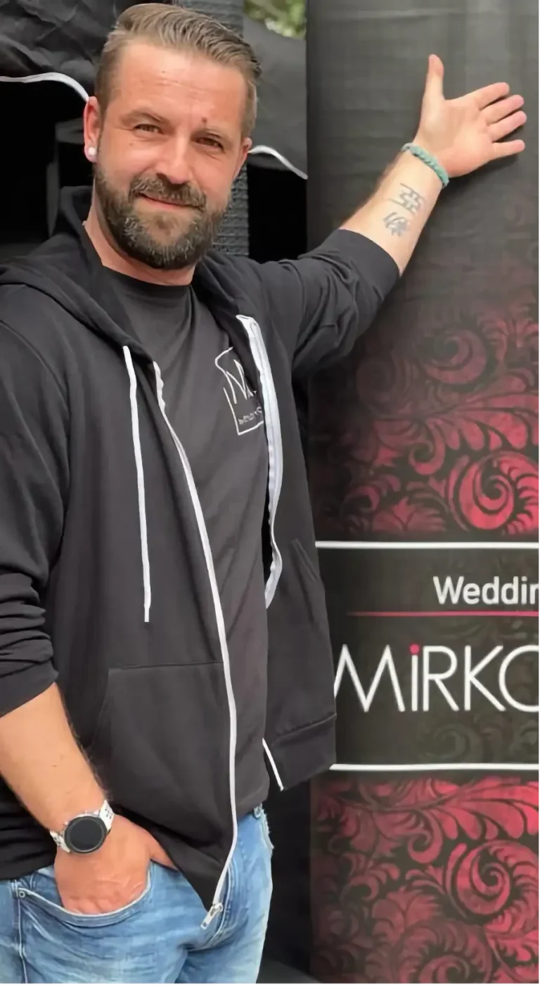 DJ Mirko Anders zeigt auf ein Werbeplakat für Hochzeitsevents.