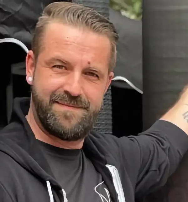 DJ Mirko Anders zeigt auf ein Werbeplakat für Hochzeitsevents.