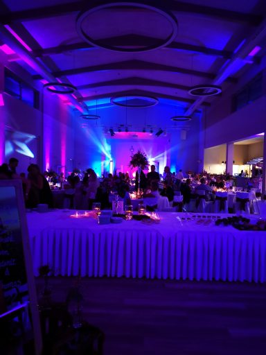 Festlich dekorierter Saal mit bunten Lichtern und gedeckten Tischen für eine Veranstaltung. Photo by DJ Mirko Anders
