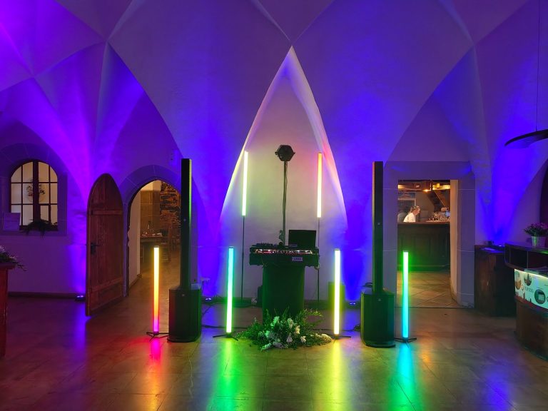 DJ Mirko Anders – Hochzeits DJ Wurzen Farbenfrohe Beleuchtung in einem Raum mit Lautsprechern und einem DJ-Pult.
