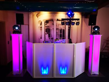 DJ-Pult mit lila und blauen Lichtern vor einer dekorativen Wand. Photo by DJ Mirko Anders