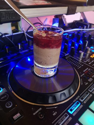Ein Glas mit Schichtdessert auf einem DJ-Pult, umgeben von Equipment. Photo by DJ Mirko Anders