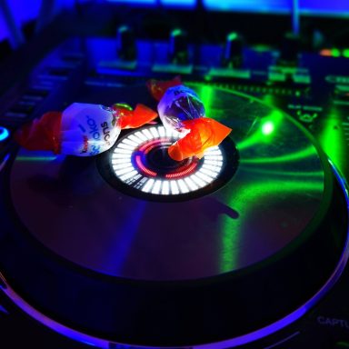 Bonbons liegen auf einem DJ-Pult, umgeben von bunten Lichtern. Photo by DJ Mirko Anders