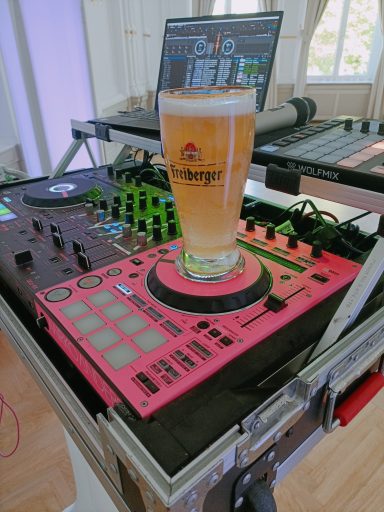 Ein Drinks steht auf einem pinken DJ-Pult mit Mischpult und Lautstärkereglern. Photo by DJ Mirko Anders