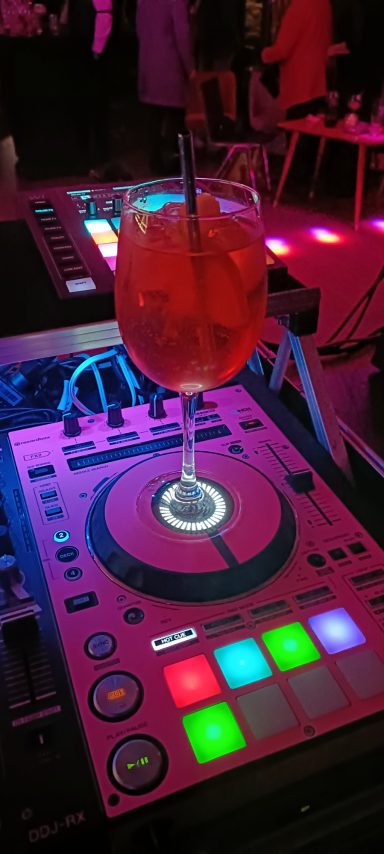 Ein Cocktailglas steht auf einem DJ-Pult mit bunten Lichtern. Photo by DJ Mirko Anders