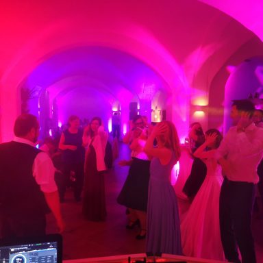 Tanzende Menschen in festlicher Kleidung unter bunten Lichtern in einem historischen Saal. Photo by DJ Mirko Anders