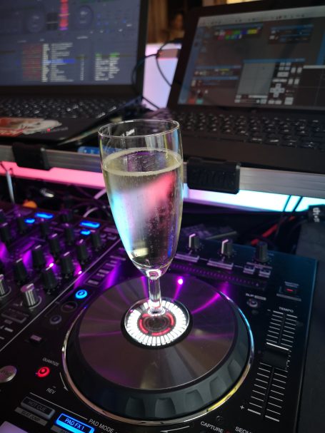 Ein Sektglas steht auf einem DJ-Controller mit bunten Lichtern. Photo by DJ Mirko Anders