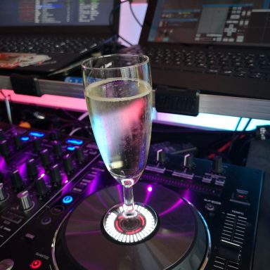 Sektglas steht auf einem DJ-Pult mit bunten Lichtern im Hintergrund.