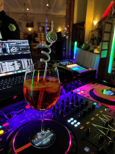 Ein Cocktailglas mit Spiralstrohhalm steht auf einem DJ-Pult mit bunten Lichtern.