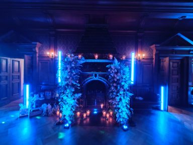 Dunkler Raum mit blauen Lichtern, Blumenbögen und Kerzen auf dem Boden. Photo by DJ Mirko Anders