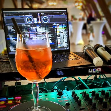 Ein Cocktailglas steht vor einem Laptop mit DJ-Software in einem festlichen Ambiente. Photo by DJ Mirko Anders