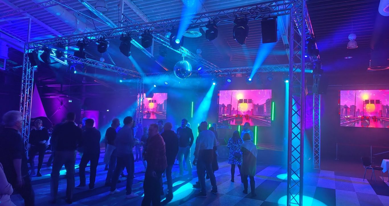 Bühne mit pinker und grüner Beleuchtung, Lautsprechern und stilvollem Hintergrund.