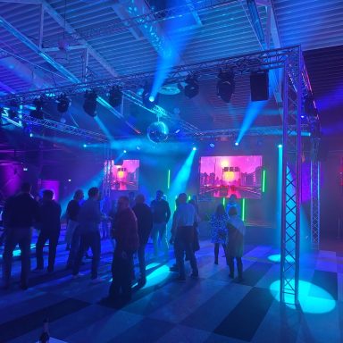 Tanzende Menschen in einem stilvollen Club mit bunten Lichtern und Disco-Kugel.