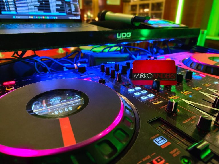DJ-Equipment mit bunten Lichtern, Plattentellern und Mischpult im Hintergrund.