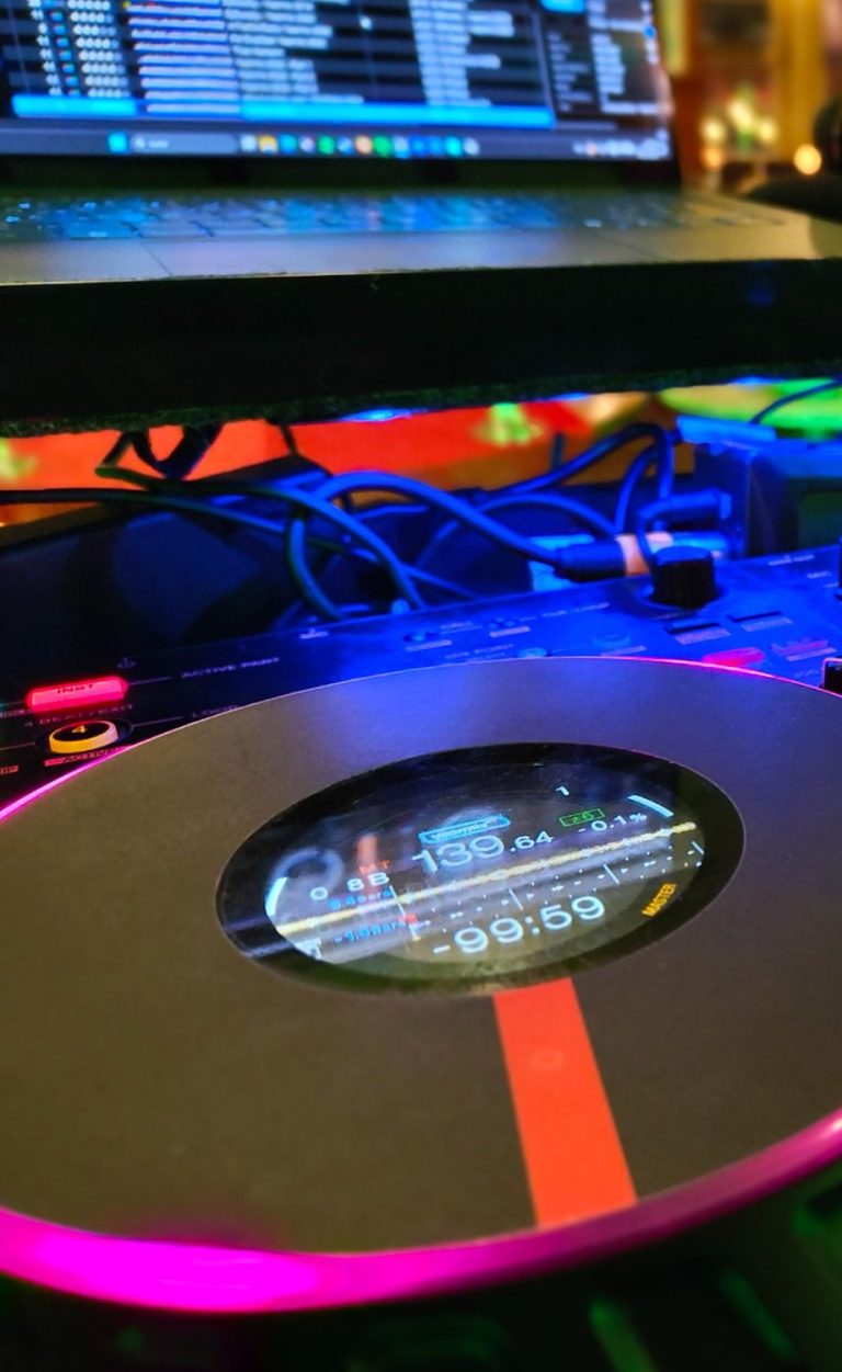 Schwarzes DJ-Deck mit bunten Lichtern und Computer im Hintergrund.