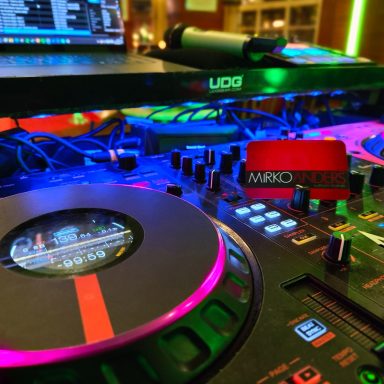 DJ-Equipment mit bunten Lichtern, Plattenspielern und Laptop im Hintergrund.
