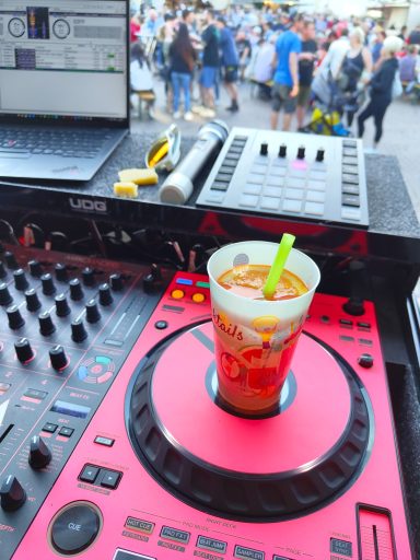 Bunte Getränkebecher auf einem DJ-Pult mit Menschenmenge im Hintergrund. Photo by DJ Mirko Anders