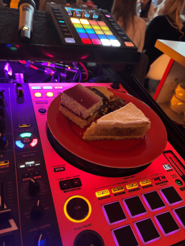 Torte auf einem Teller, platziert auf einem DJ-Pult mit bunten Lichtern und Tasten.