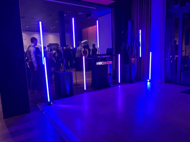 Blaue Lichtstäbe markieren den Eingangsbereich zu einer Veranstaltung mit Menschen.