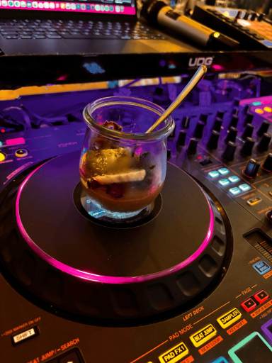 Glas mit dunklem Getränk und Strohhalm auf einem DJ-Deck mit bunten Lichtern.