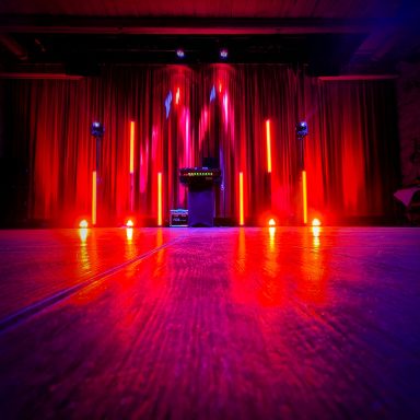 Dunkle Bühne mit roten und lila Lichtern sowie Vorhängen im Hintergrund. Photo by DJ Mirko Anders
