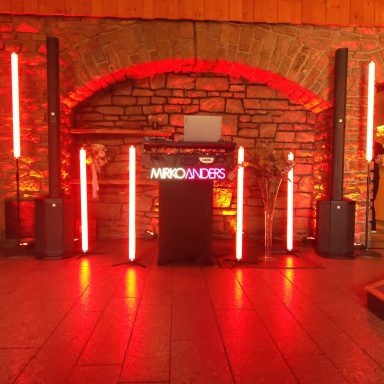 Dunkler Raum mit rotem Licht, DJ-Pult und Lautsprechern vor einer Steinmauer.