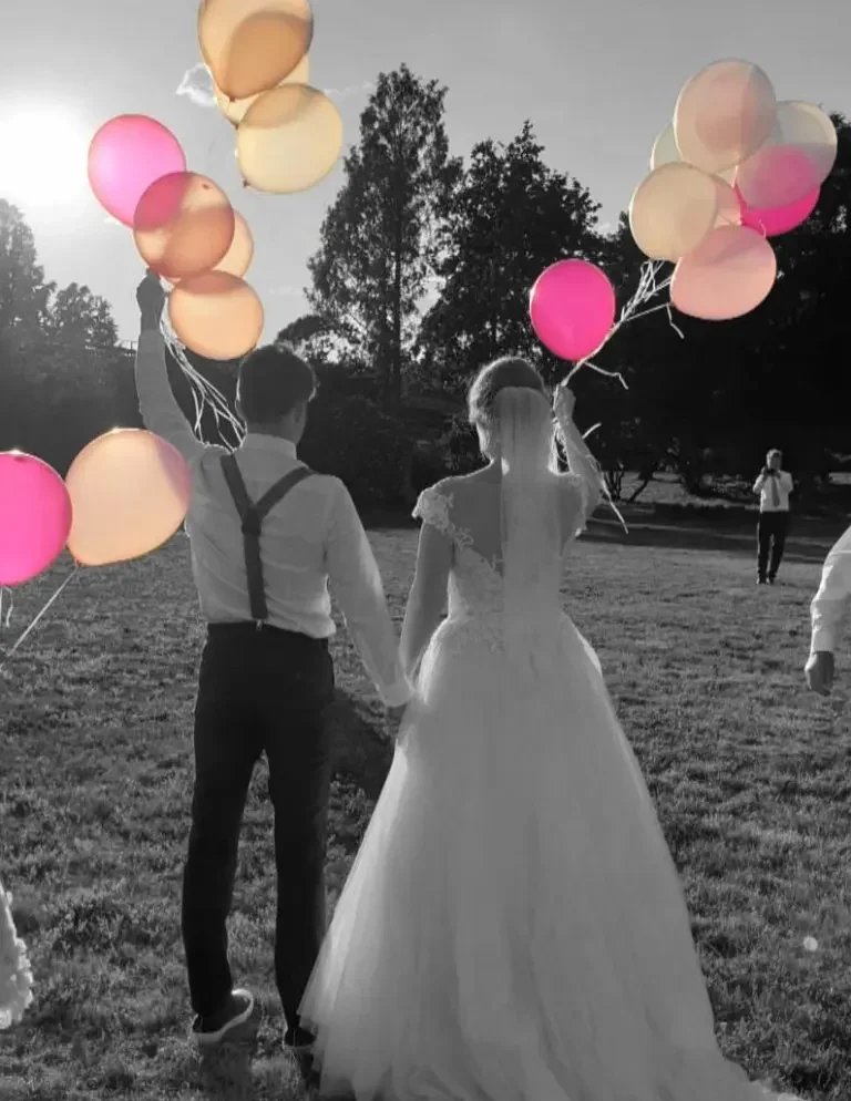 Hochzeitspaar hält bunten Ballons beim Sonnenuntergang auf einer Wiese.