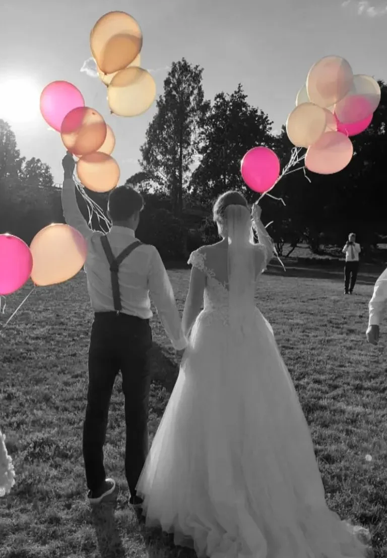 Hochzeits-DJ Leipzig Mirko Anders Hochzeitspaar hält bunten Ballons beim Sonnenuntergang auf einer Wiese.