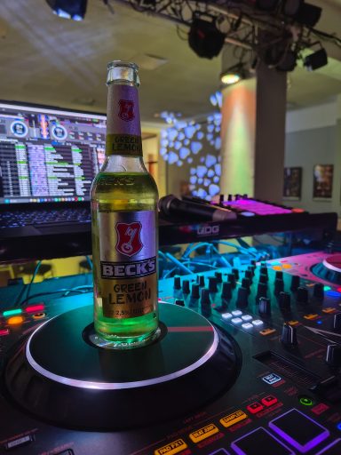 Flasche Bier steht auf einem DJ-Pult mit bunten Lichtern im Hintergrund. Photo by DJ Mirko Anders
