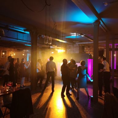 Tanzende Menschen in einer beleuchteten Location mit bunten Lichtern und Nebel.