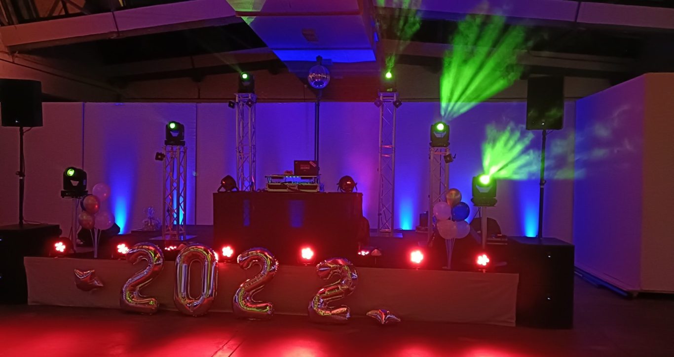 Bühne mit pinker und grüner Beleuchtung, Lautsprechern und stilvollem Hintergrund.