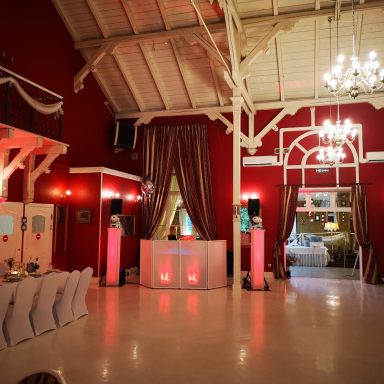 Festlicher Saal mit roten Wänden, Tischen, Beleuchtung und einem DJ-Pult.  Photo by DJ Mirko Anders