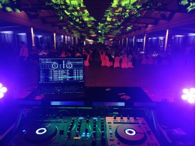 DJ-Pult mit bunten Lichtern, Blick auf einen festlich dekorierten Saal. Photo by DJ Mirko Anders