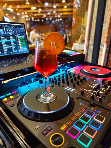 Cocktailglas auf einem DJ-Pult mit bunten Lichtern und Musiksoftware im Hintergrund. Photo by DJ Mirko Anders