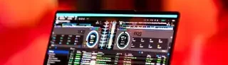 Laptop mit DJ-Software, umgeben von warmem, gefiltertem Licht und unscharfen Menschen.