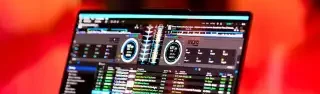 DJ Mirko Anders – Hochzeit Laptop mit DJ-Software, umgeben von warmem, gefiltertem Licht und unscharfen Menschen.